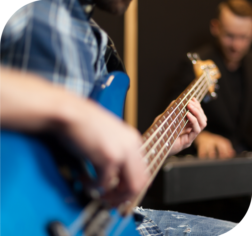 Close-up of a student playing bass guitar during a music lesson in a recording studio setting.