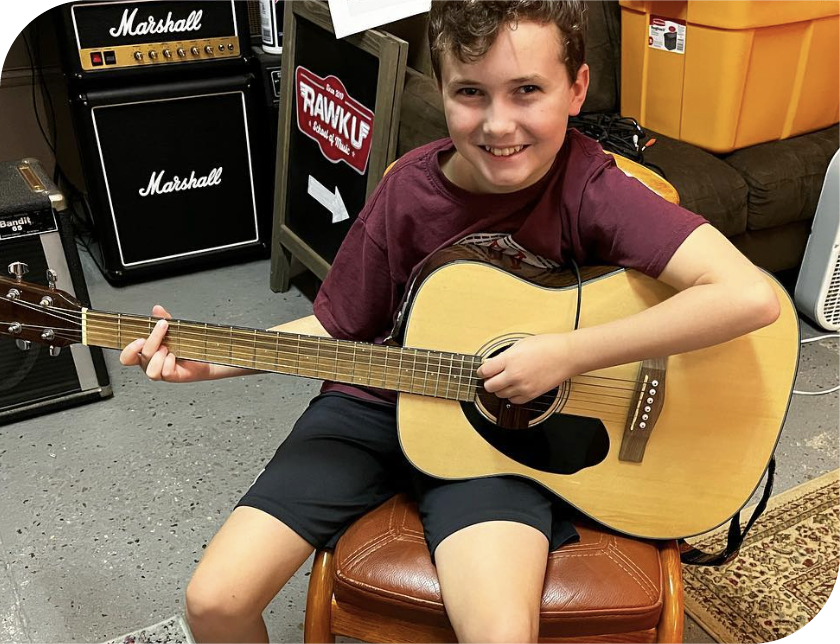 Smiling youth student holding acoustic guitar during music lesson at Rawk U with Marshall amplifier visible in professional teaching studio