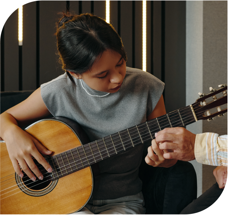 Music instructor teaching a young student proper finger placement during a guitar lesson.