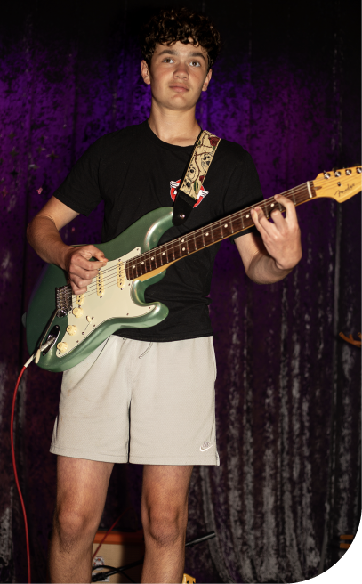 Teenage student performing on stage with an electric guitar during a live music showcase.